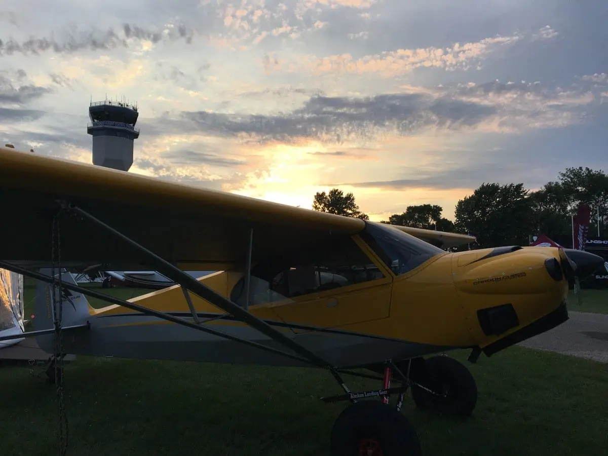 A yellow airplane parked on the grass at sunset.